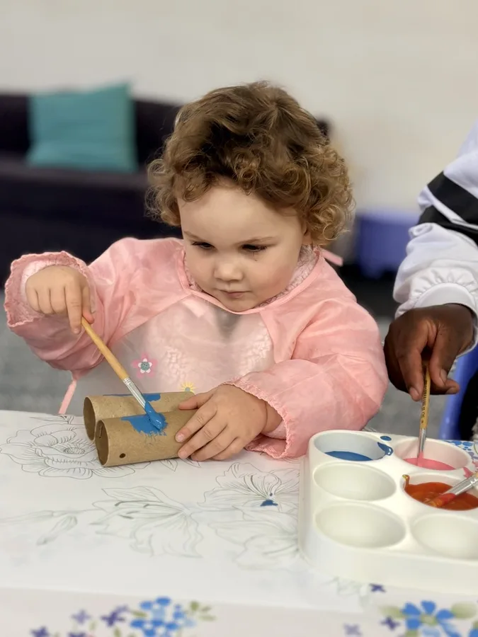A child painting while a caregiver works alongside them