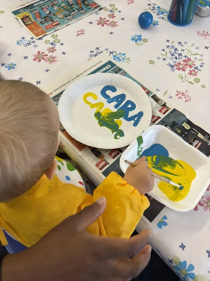 A caregiver and child painting together during a morning activity