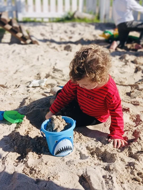 A toddler playing with a bucket in the sand